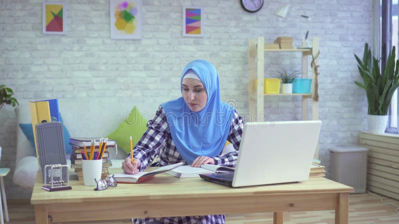 Όμορφη νέα μουσουλμανική γυναίκα στο hijab, που μελετά στα σύγχρονα διαμερίσματα